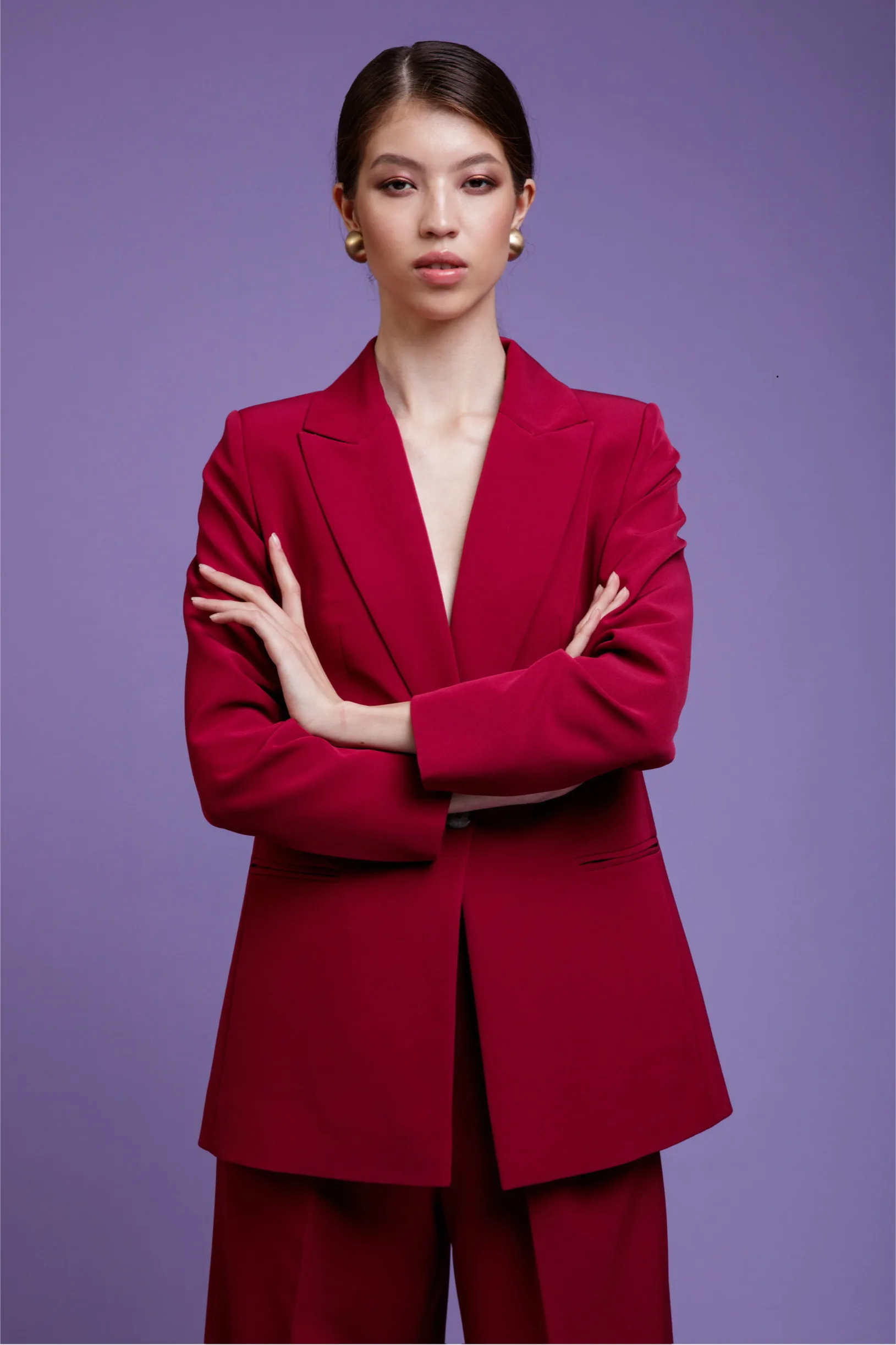 Fashion photo of a beautiful elegant young asian woman in a pretty red oversized suit, jacket, pants posing over purple, lavender, lilac background. Studio Shot.